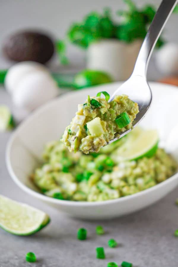 A silver fork full of avocado egg salad garnished with chopped green onions.
