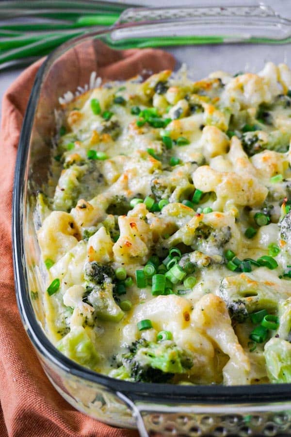 Freshly baked creamy cauliflower casserole with broccoli topped with chopped green onion in a glass baking dish.