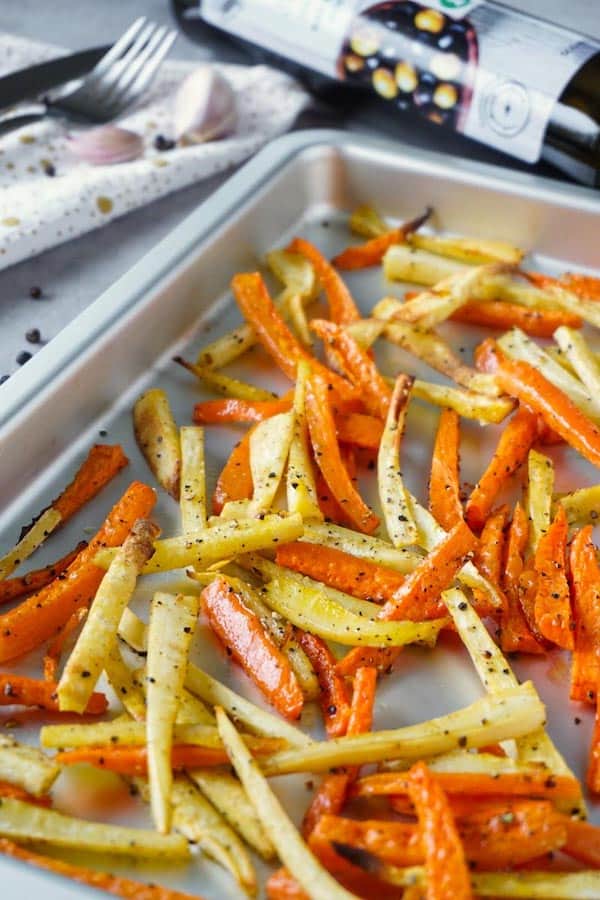 Roasted in olive oil with salt and ground black pepper carrots and parsnips on a silver baking tray.