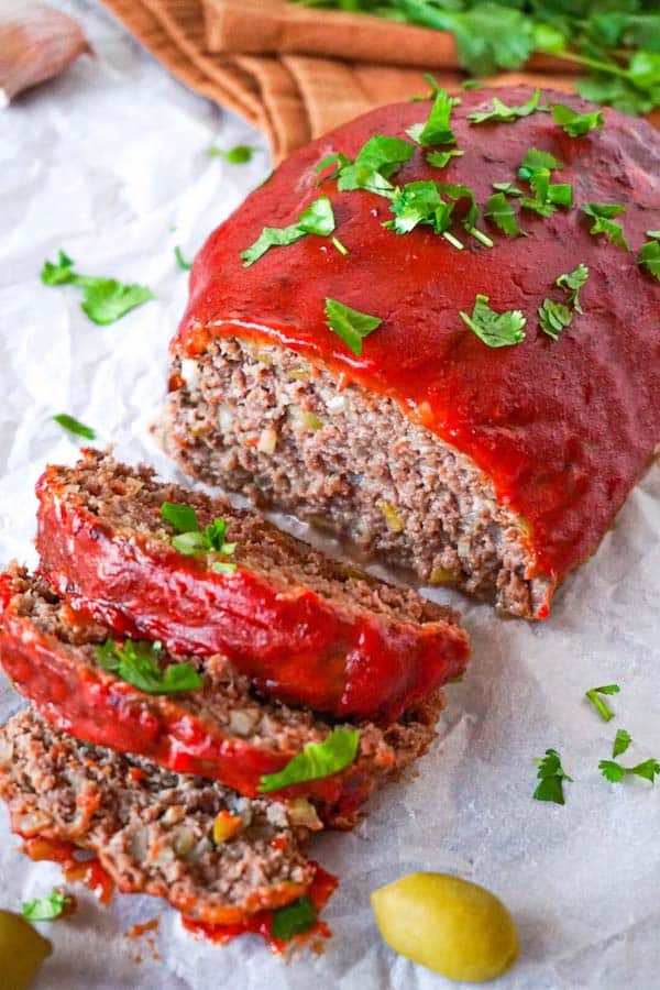 Sliced keto meatloaf on a white parchment paper covered with spicy tomato glaze and garnished with chopped cilantro.