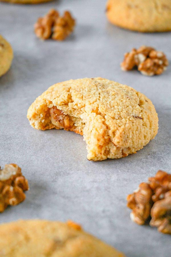 Freshly baked cookie with walnuts lying on a grey kitchen top, one bite taken.