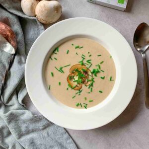 Creamy mushroom soup garnished with freshly chopped chives and fried mushroom slices in a white soup bowl.