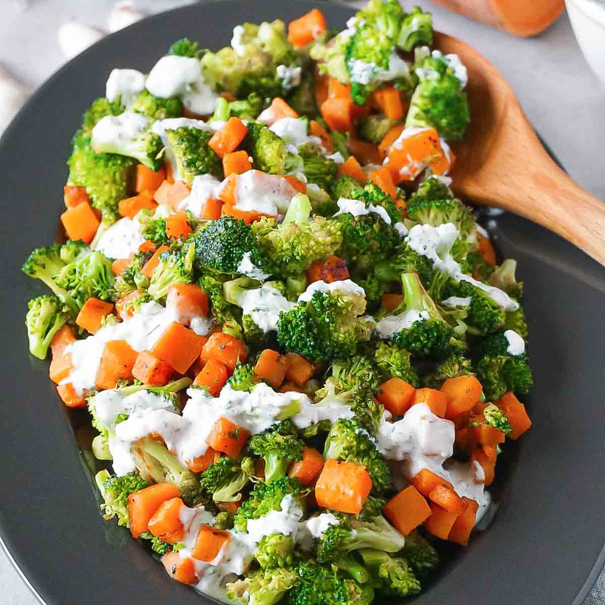 Oval plate full of broccoli with sweet potatoes, topped with creamy garlic ranch with dill.