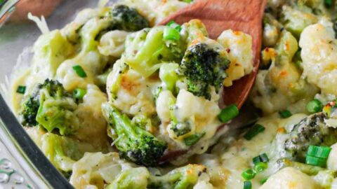 Close up of a wooden spoon scooping out creamy cauliflower with broccoli from a glass baking dish.