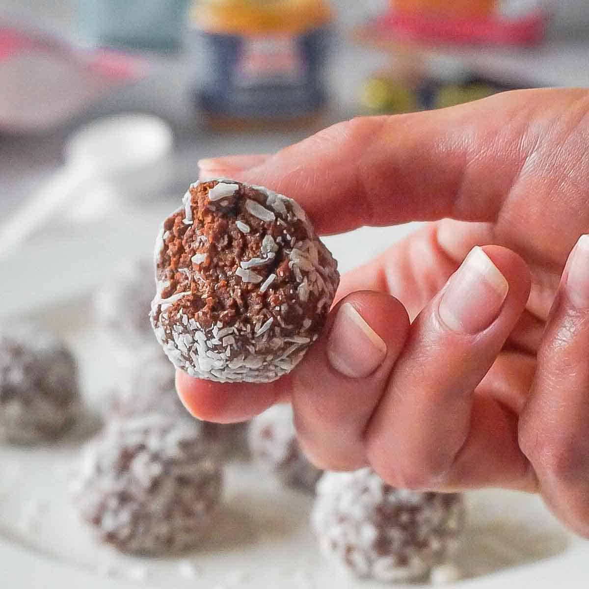 A hand holding brownie bliss ball covered in coconut flakes, one bite taken.