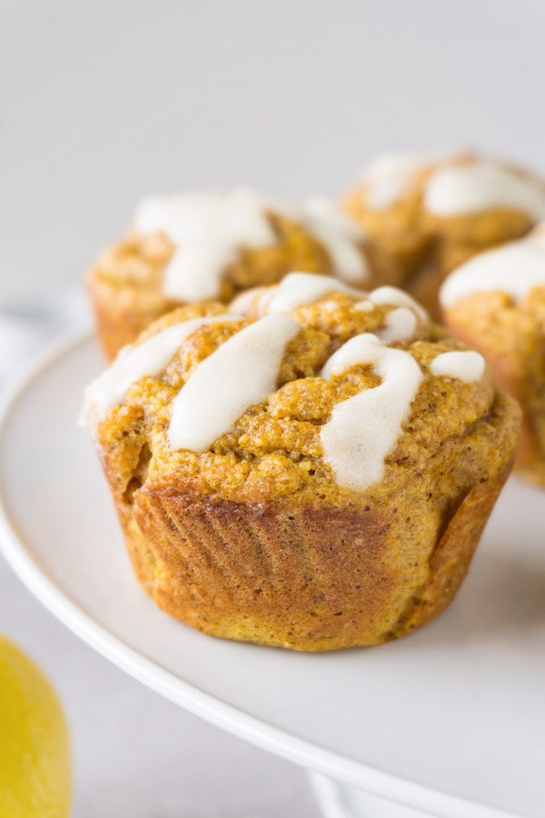 Almond flour pumpkin muffins drizzled with white icing on top lying on a white footed cake platter.