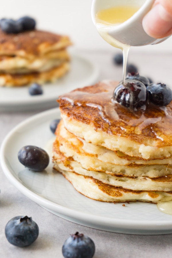 Cottage cheese pancake tower with topped with fresh blueberries, keto-friendly syrup pouring on top.