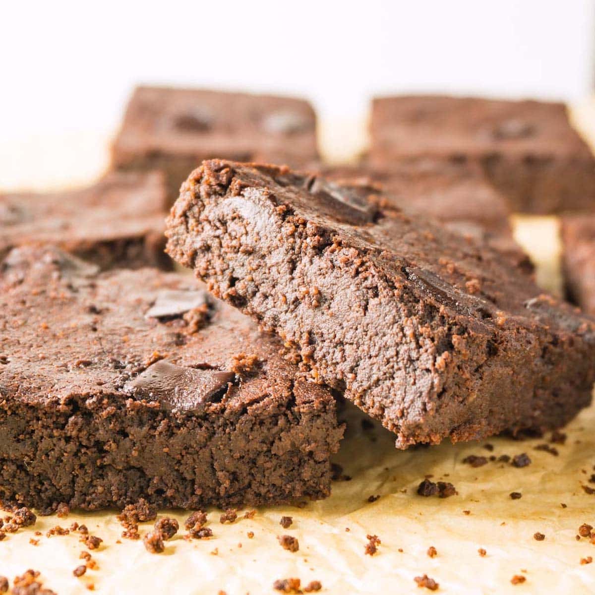 Close up image of fudge brownies on a brown parchment paper, more brownies on the background.