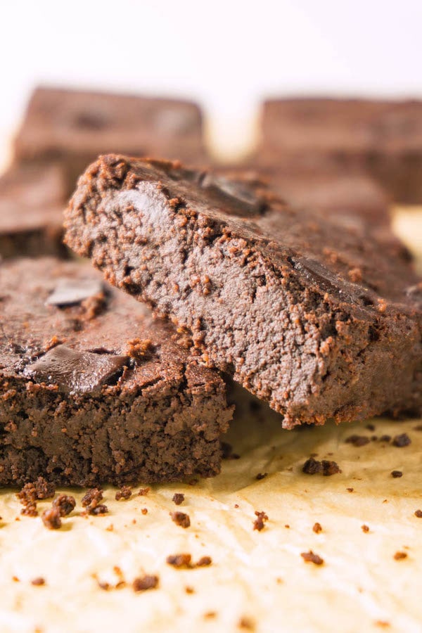 Two sliced fudge brownies on a brown parchment paper, more brownies on the background.