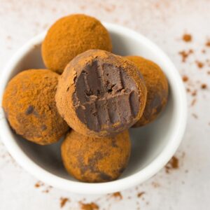 A small white bowl filled with chocolate truffles dusted in cocoa powder, one bite taken from the top one.