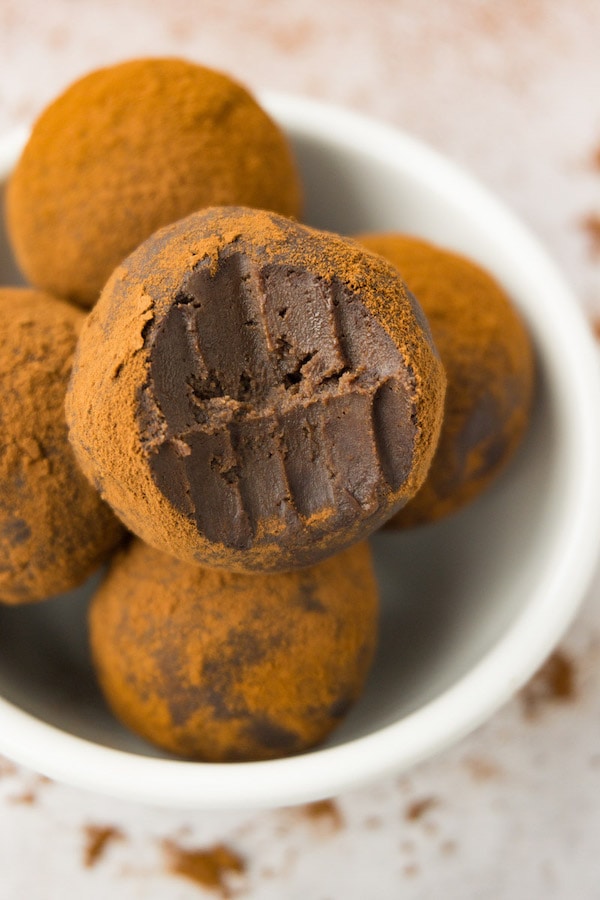 Low carb chocolate truffles dusted in cocoa powder in a small, round, white bowl, one bite taken from one of the truffles.