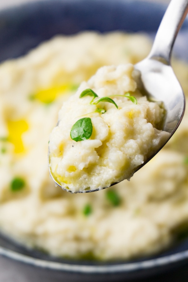 A silver spoon with mashed cauliflower, melted butter and thyme leaves.