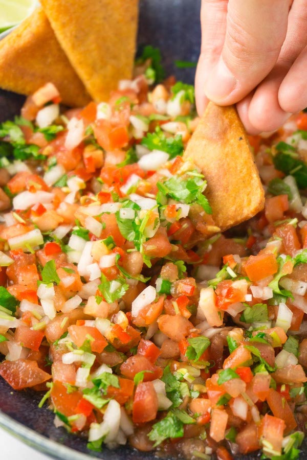 Dipping tortilla chips into a bowl filled with salsa.