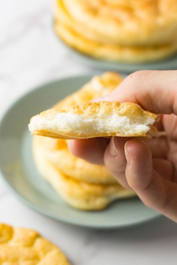 A hand holding a piece of a cloud bread roll.