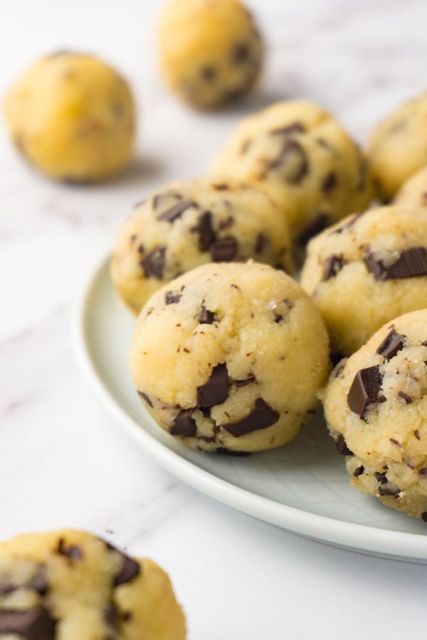 Edible cookies dough balls with chocolate chips on a small round plate. more balls are lying around.