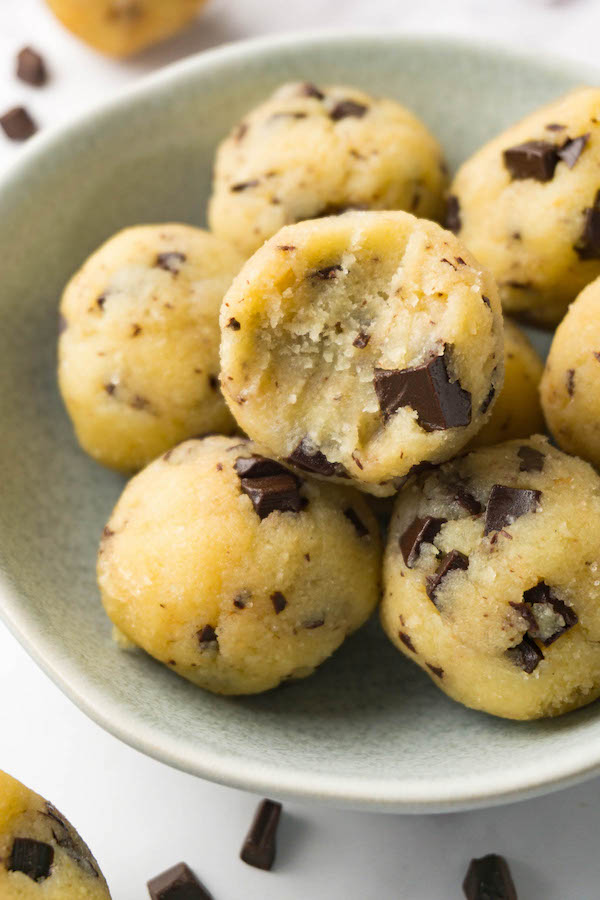 A small bowl filled with edible cookie dough balls, one bite taken from the top one.