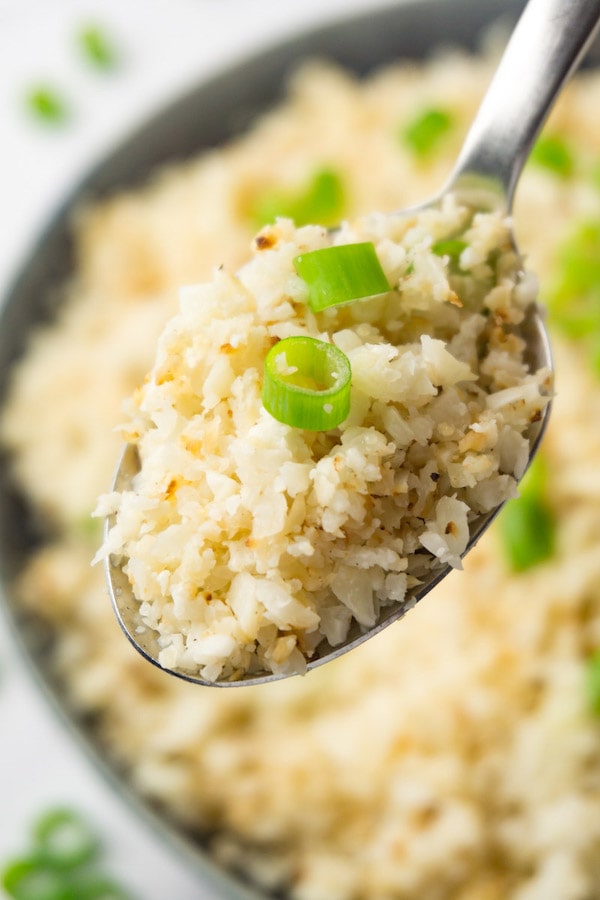 A spoon full of cauliflower rice topped with fresh spring onions.