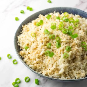 A close up shot of a large blue bowl filled with fluffy cauliflower rice garnished with freshly-chopped spring onions.