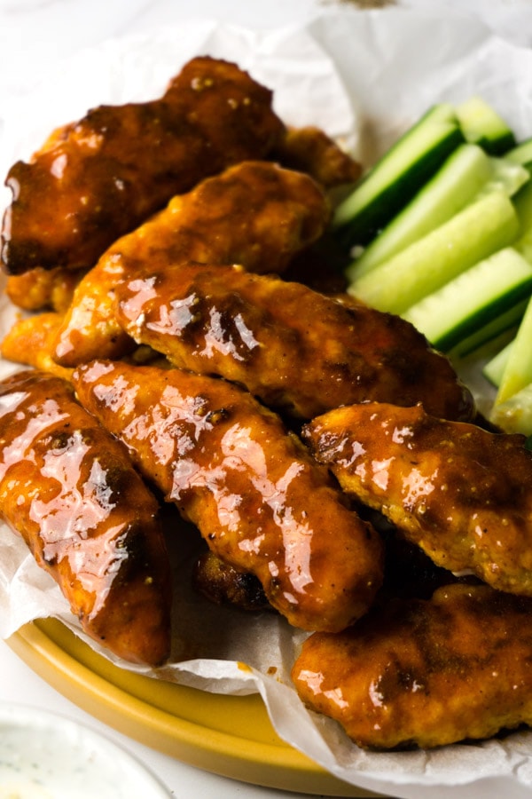 Chicken tenders covered with buffalo sauce, cucumber sticks on the background.