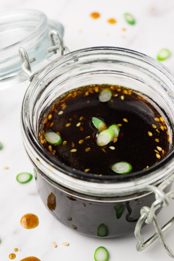 A glass jar filled with teriyaki sauce topped with sesame seeds and green onions.