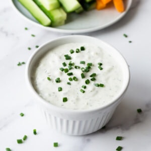 A close up shot of a small round white bowl with blue cheese dipping sauce garnished with freshly chopped chives.