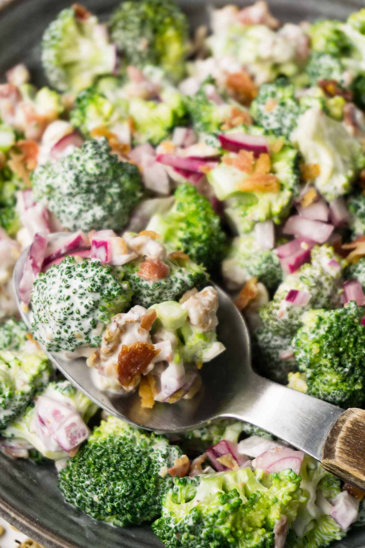 Spoon filled with broccoli with bacon and onions salad lying in the salad bowl.