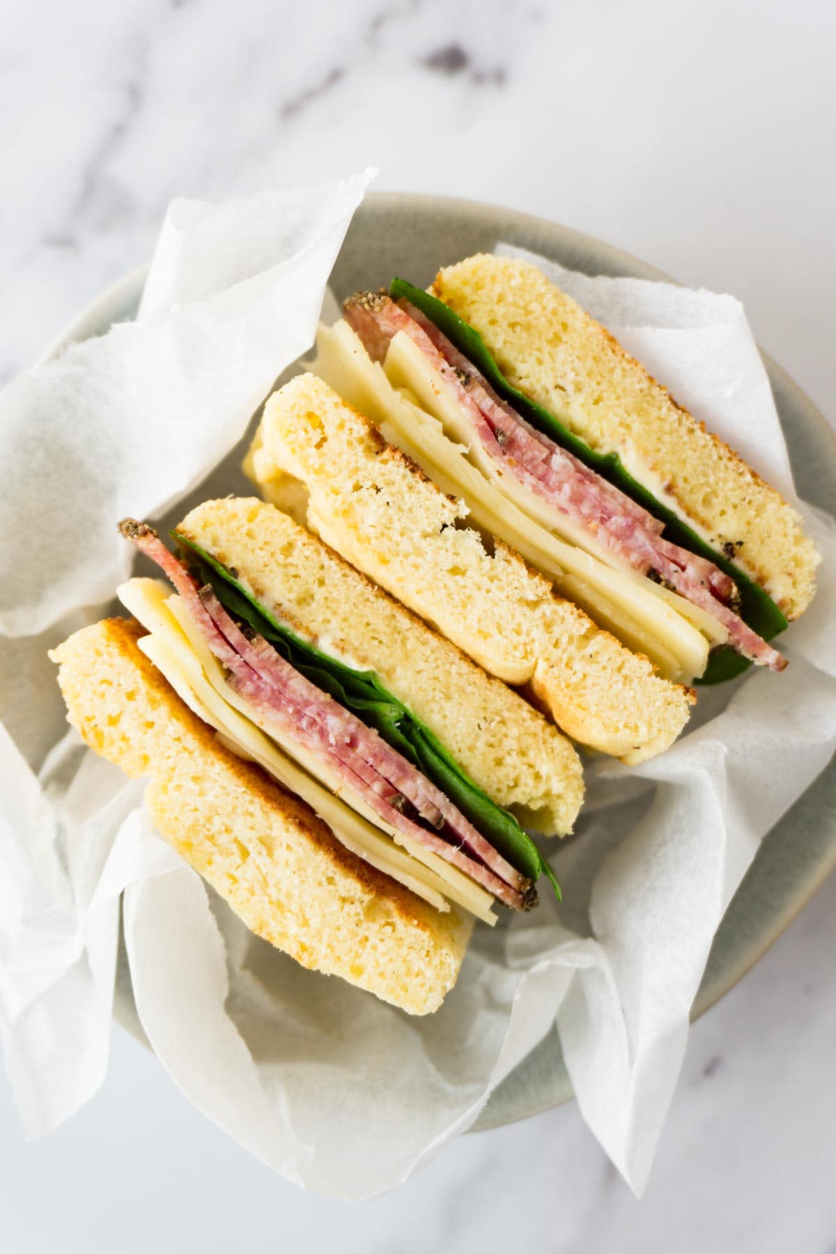 Two sandwiches with cheese, spinach, salami and keto bread in a small round bowl.