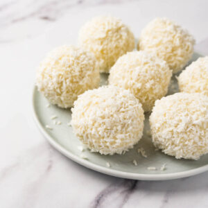 Cream cheese coconut balls covered in shredded coconut on a small round plate.