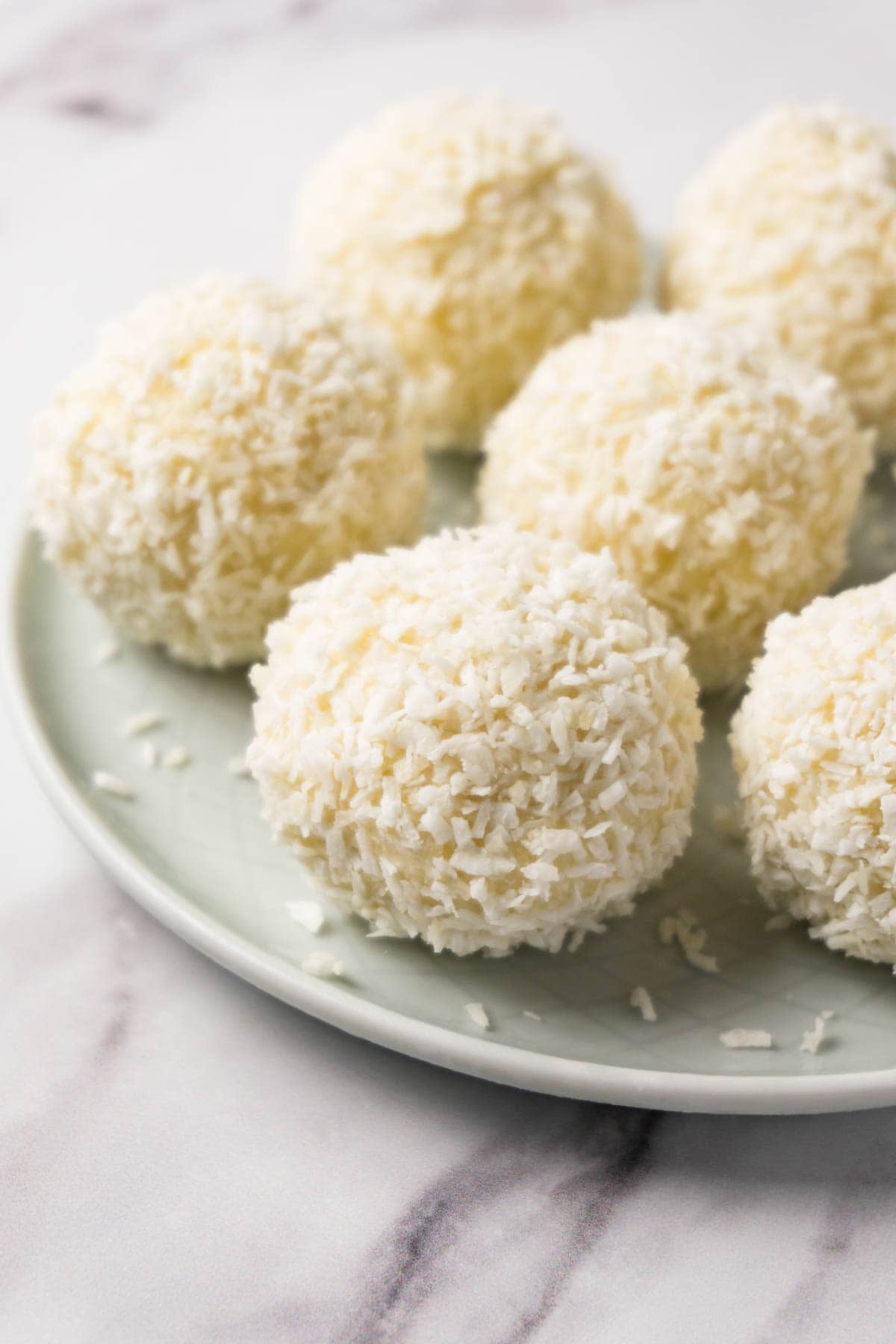 Closeup shot of a small round plate with coconut balls covered in shredded coconut.