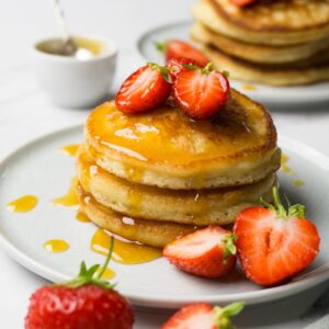 Three pancakes stacked one on top of each other, topped with fresh strawberries and sugar-free syrup.