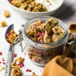 An opened glass jar filled with nuts and seeds granola with dried raspberries.