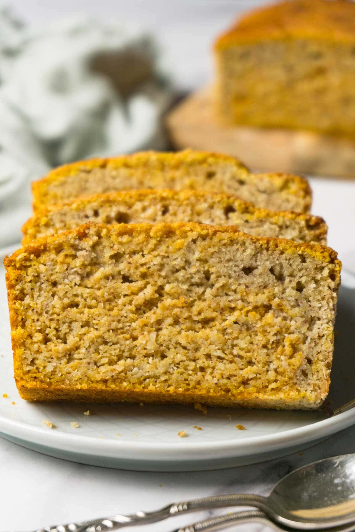 Three slices of low carb pumpkin bread served on a small round plate with silver spoons lying near.