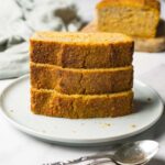 Tower of pumpkin bread slices served on a round plate, a loaf of bread on the background.
