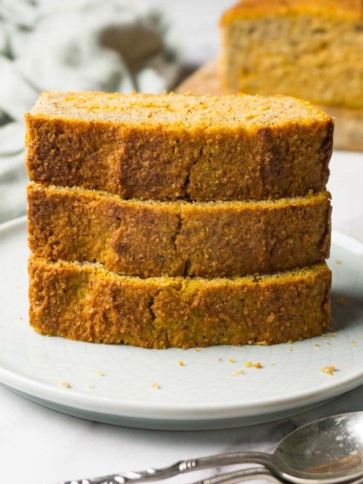 Tower of pumpkin bread slices served on a round plate, a loaf of bread on the background.