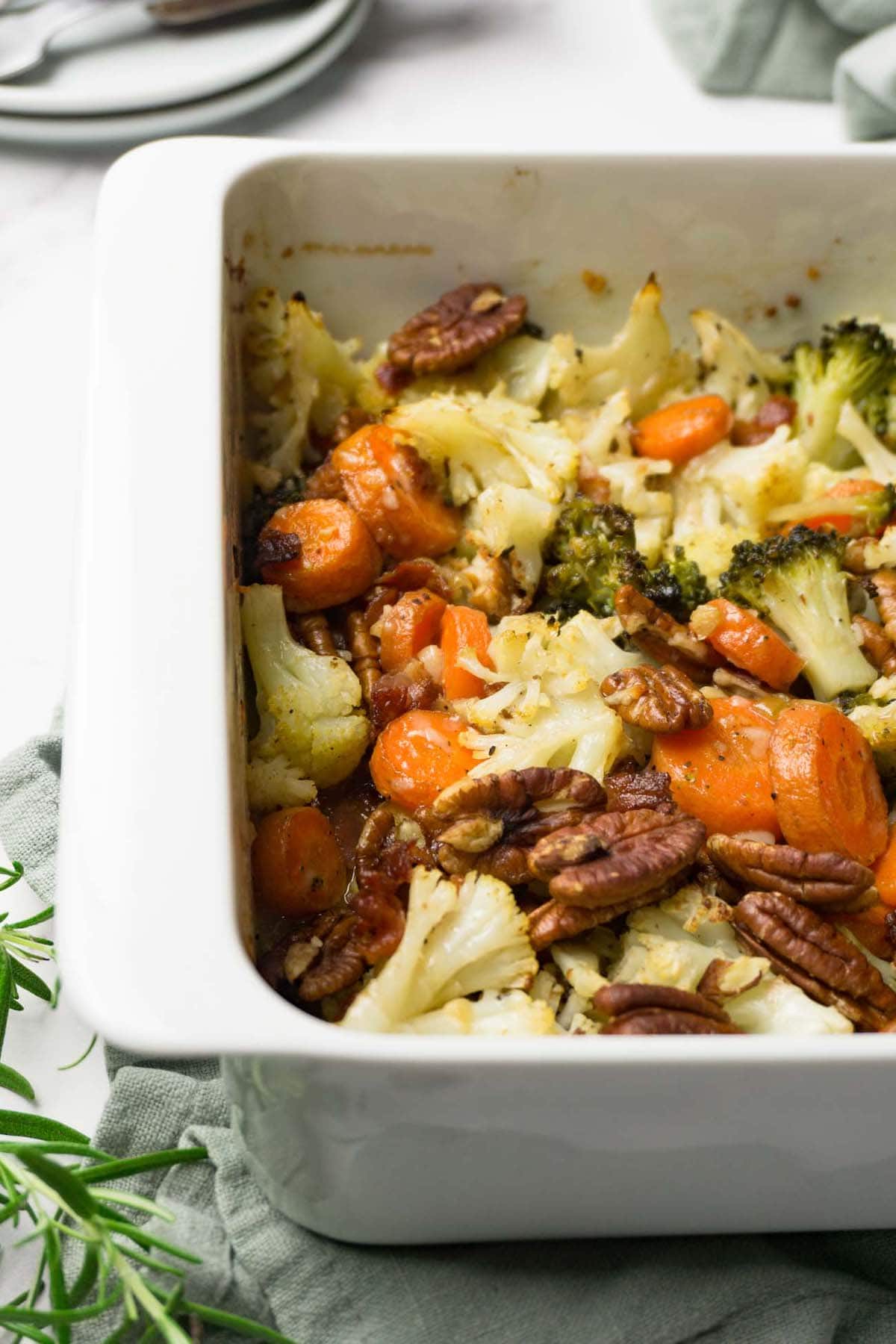 Close up shot of a white casserole dish with cauliflower stuffing with broccoli, carrots, pecans and bacon bits.