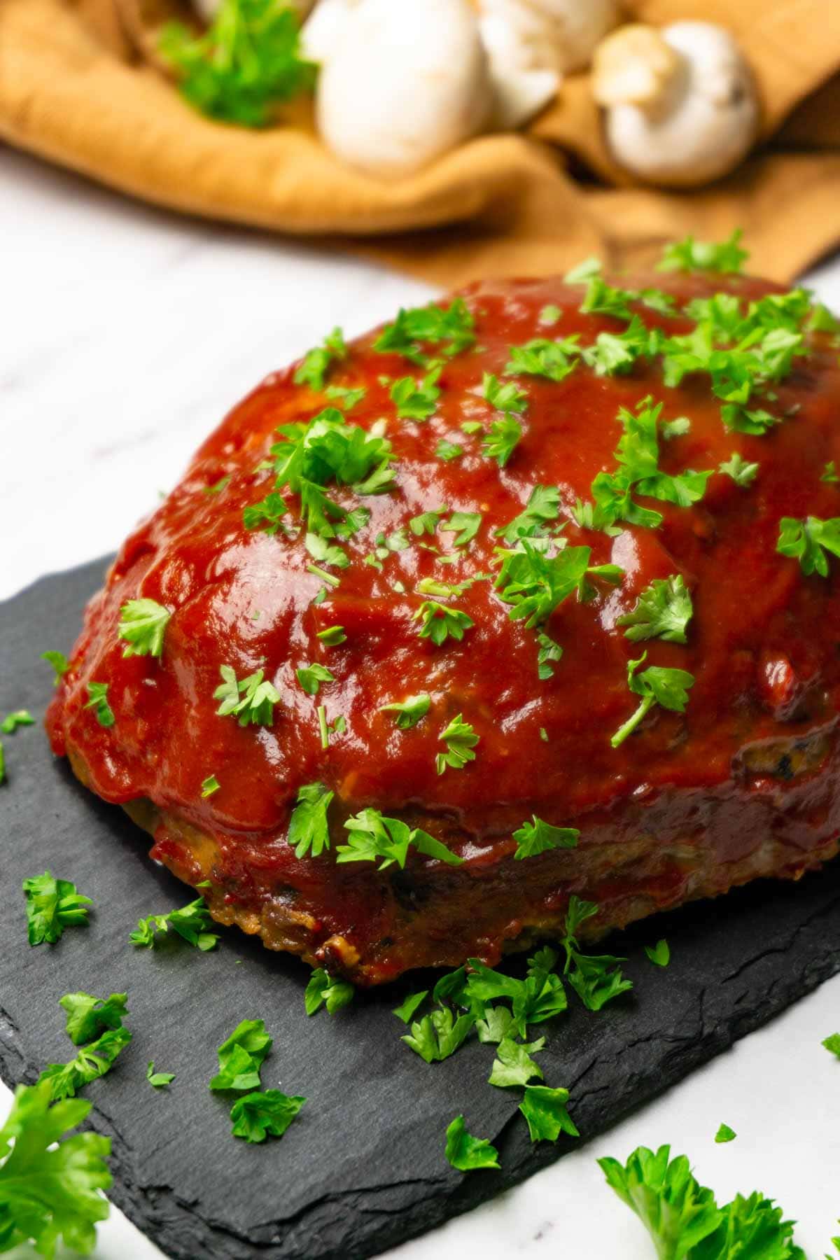 Turkey meatloaf with ketchup glaze garnished with fresh parsley served on a black stone board.