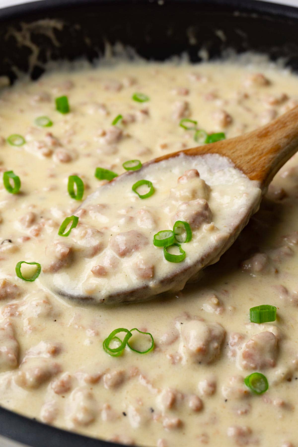 A skillet filled with sausage gravy garnished with freshly chopped green onions.
