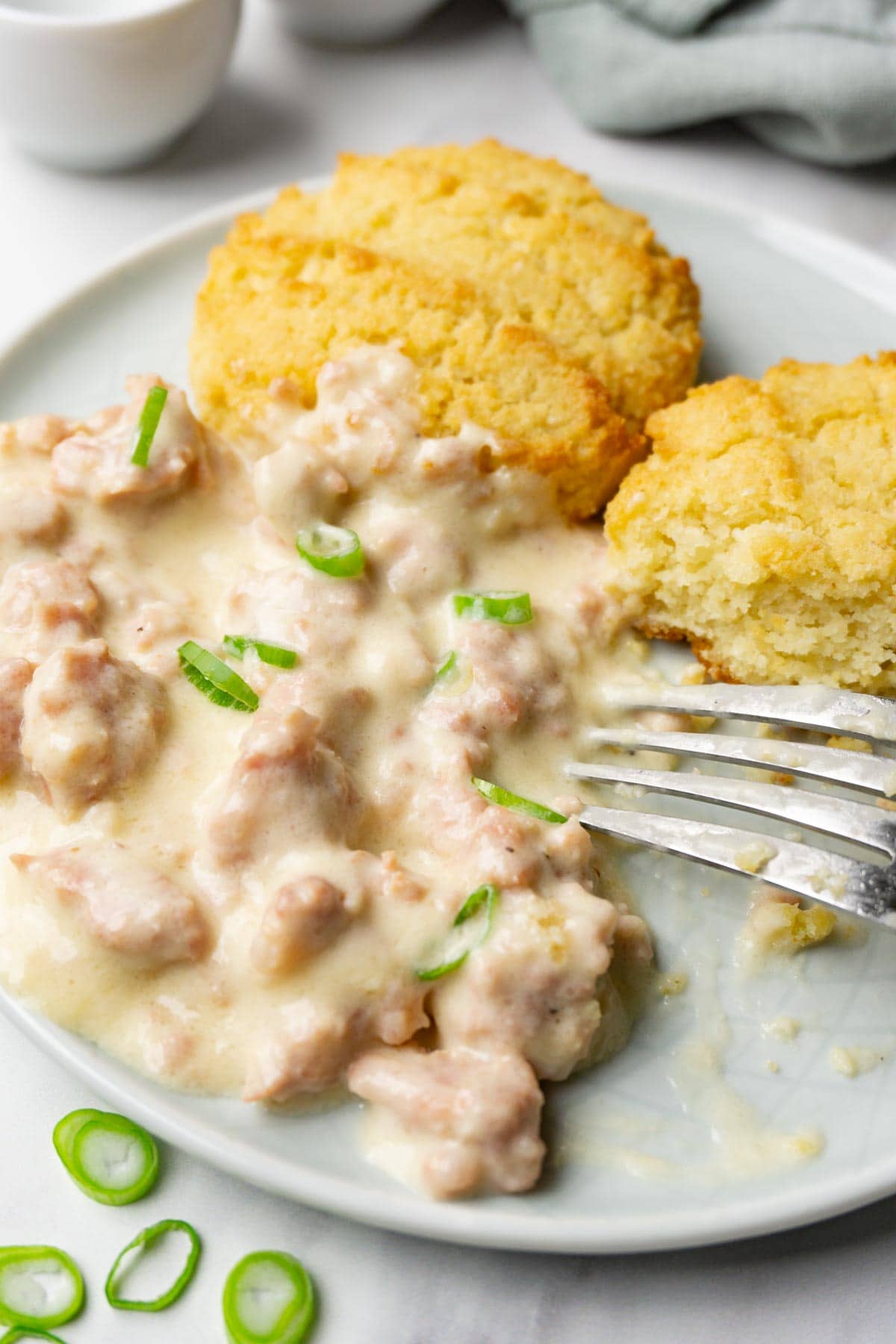 Biscuits and sausage gravy on a plate, one bite taken from one of the biscuits with some gravy.