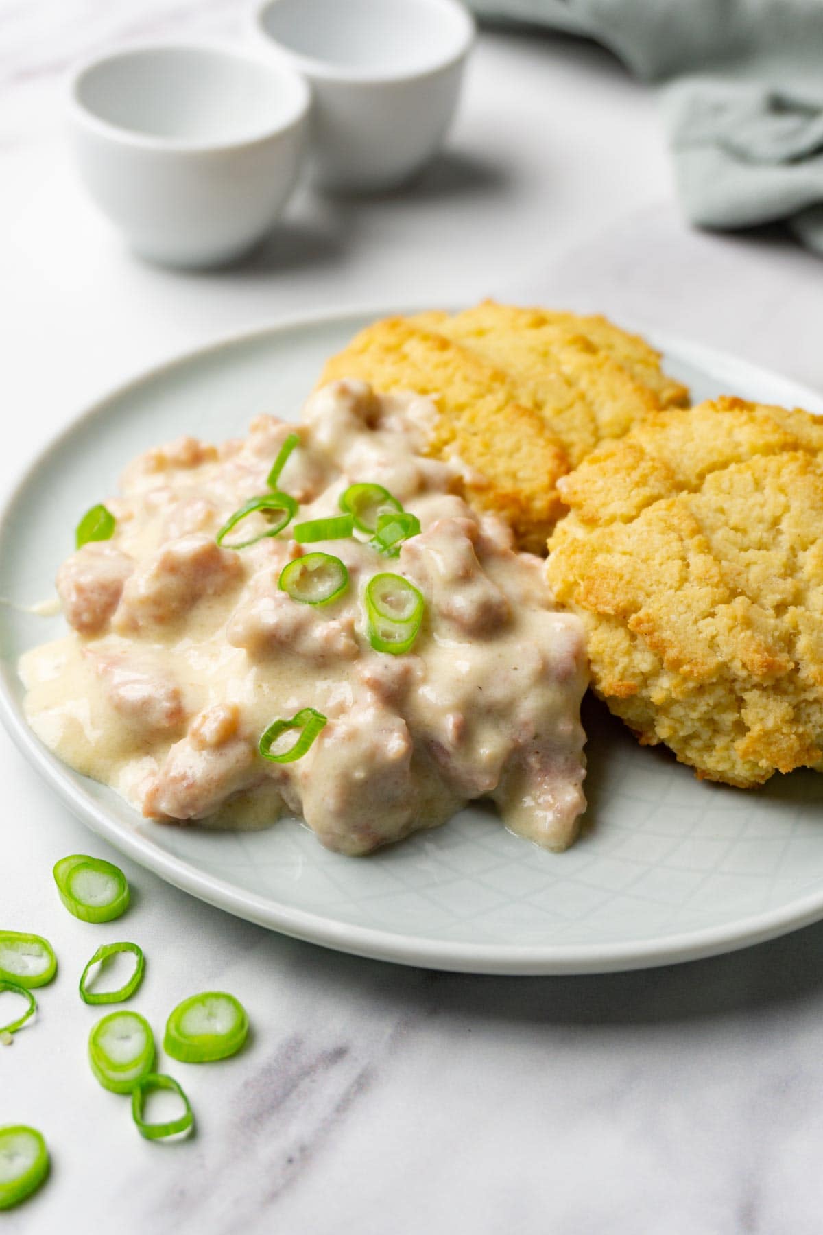 Asmall plate with biscuits and sausage gravy garnished with chopped green onion.