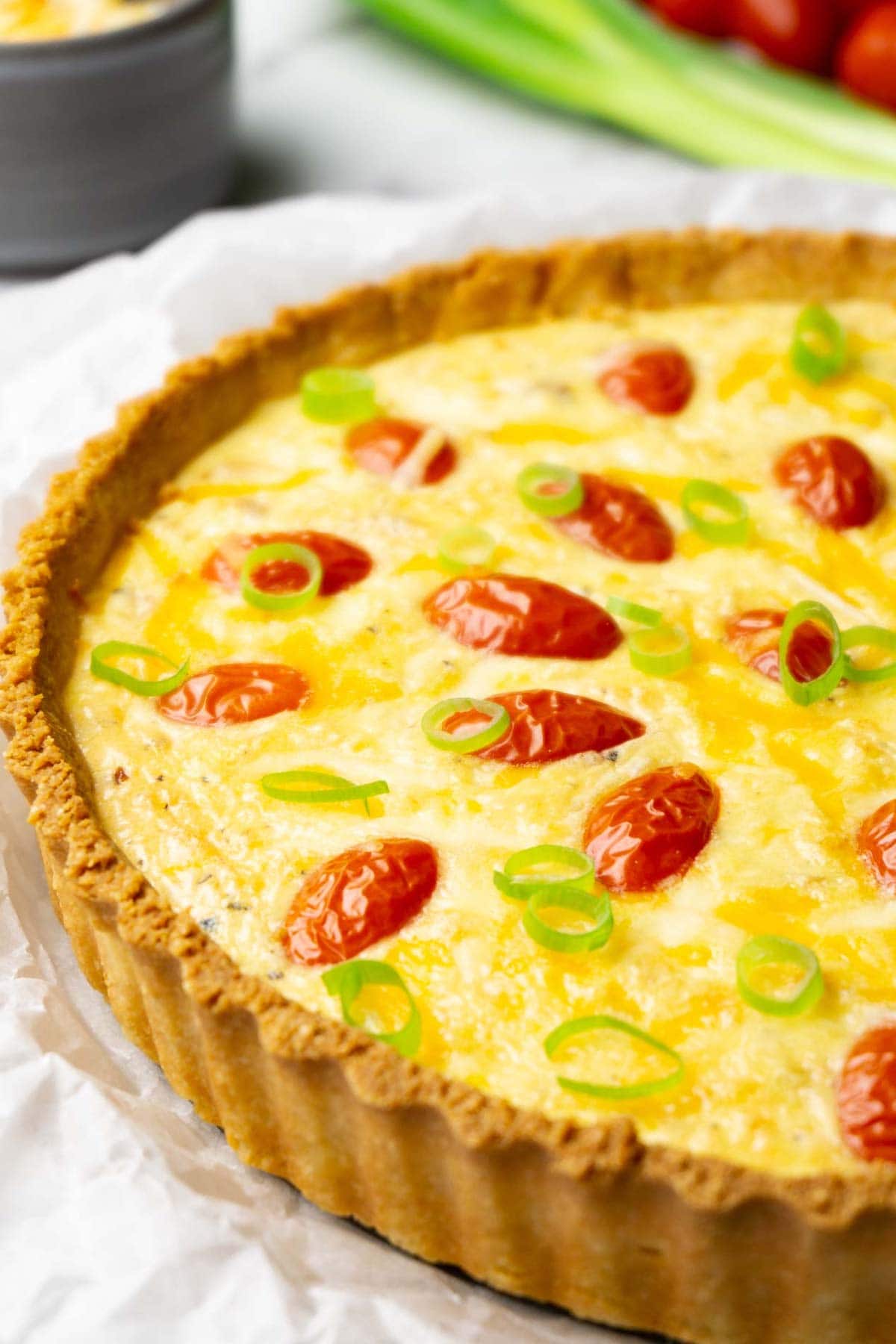 Close up shot of a quiche with chicken topped with halved cherry tomatoes, melted cheese and freshly chopped green onions.