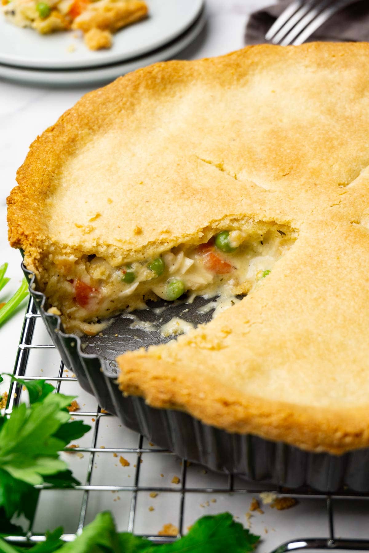 Chicken pot pie in a pie dish standing on a cooling rack, one slice taken.