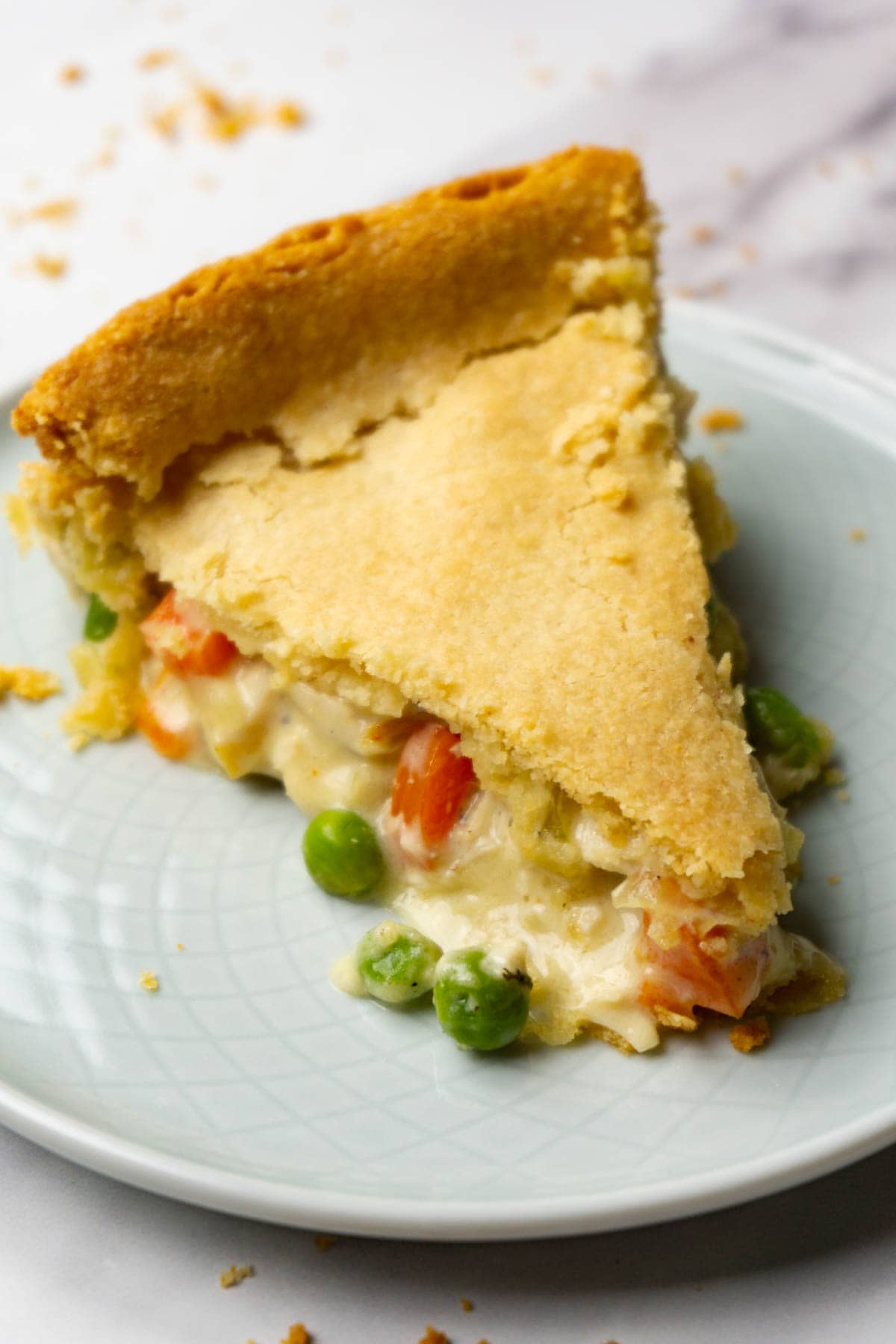 A slice of chicken pot pie with green peas, carrots, and chicken on a small round plate.