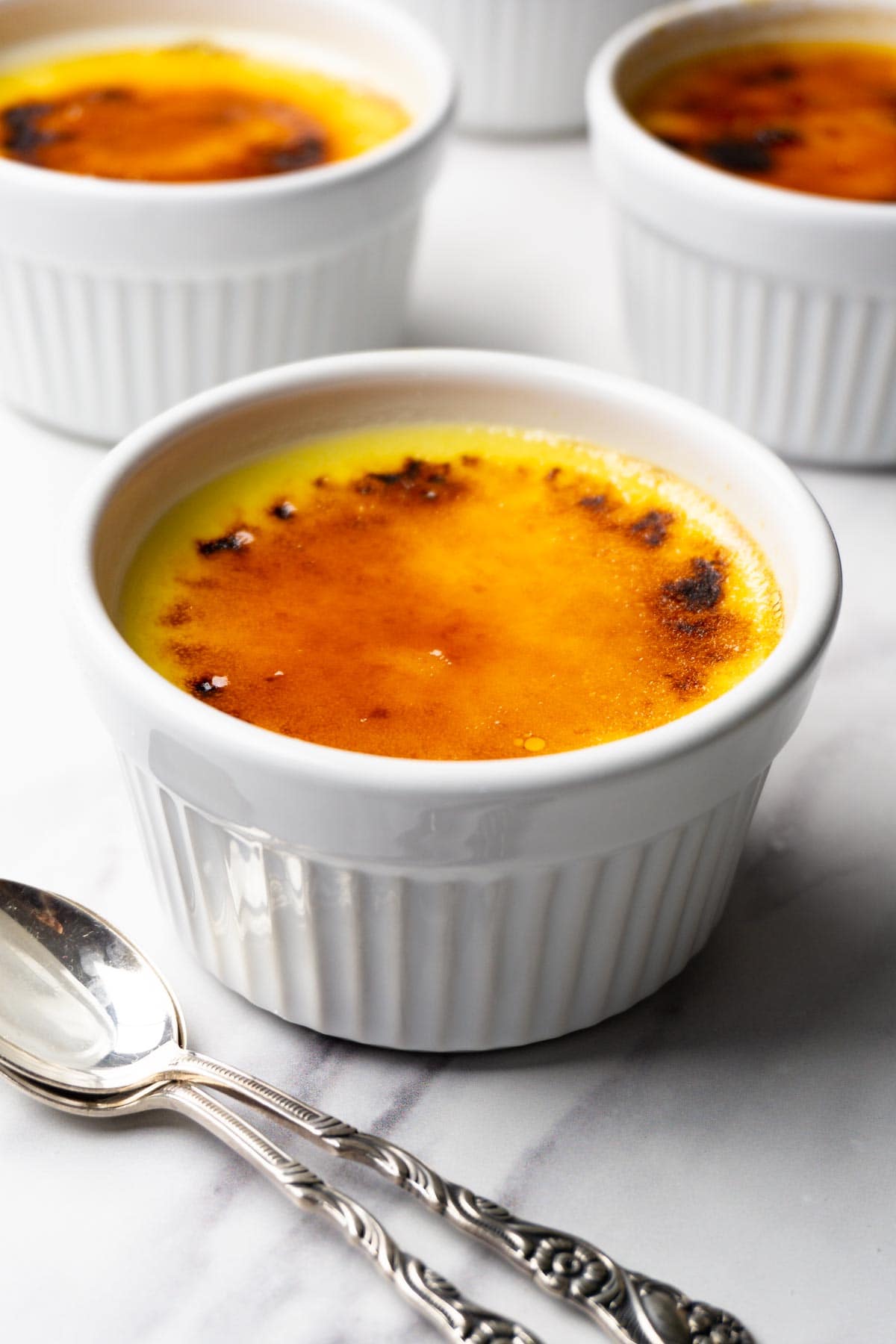 White ramekin with vanilla creme brûlée, two spoons are lying next to it.