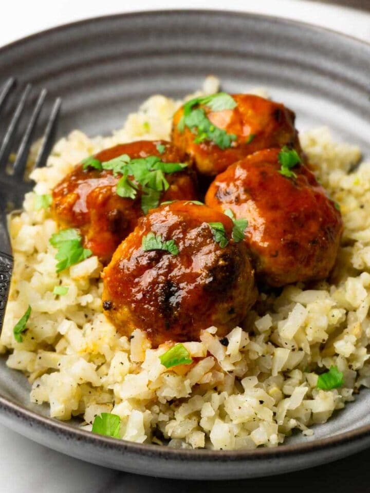 Close up picture of chicken meatballs in buffalo sauce served with cauliflower rice.