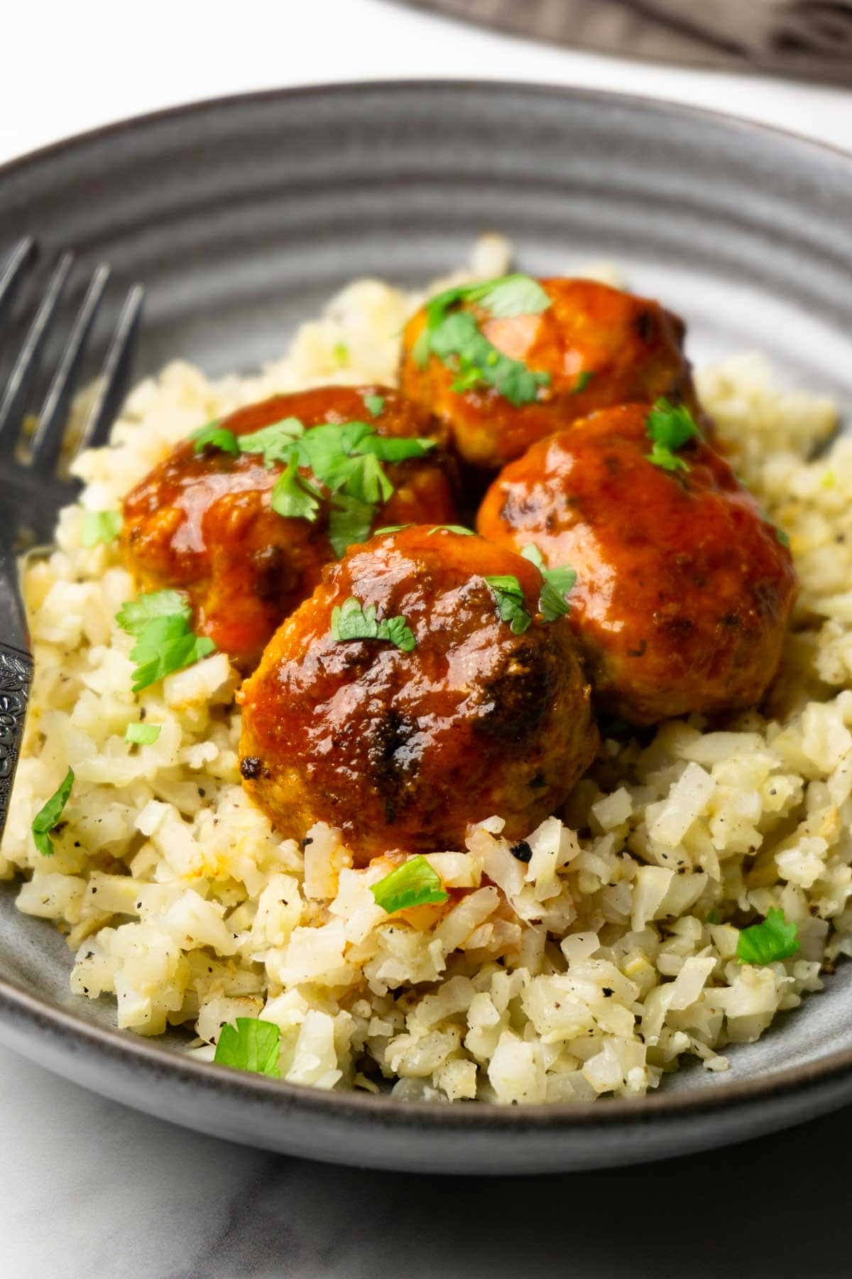 Buffalo chicken meatballs garnished with freshly chopped served on a cauliflower rice pillow in a grey bowl.