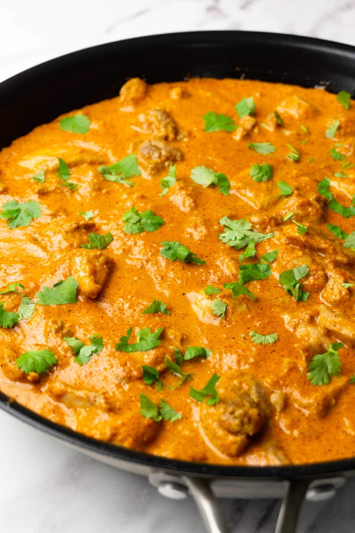 Butter chicken in a frying pan garnished with fresh cilantro.