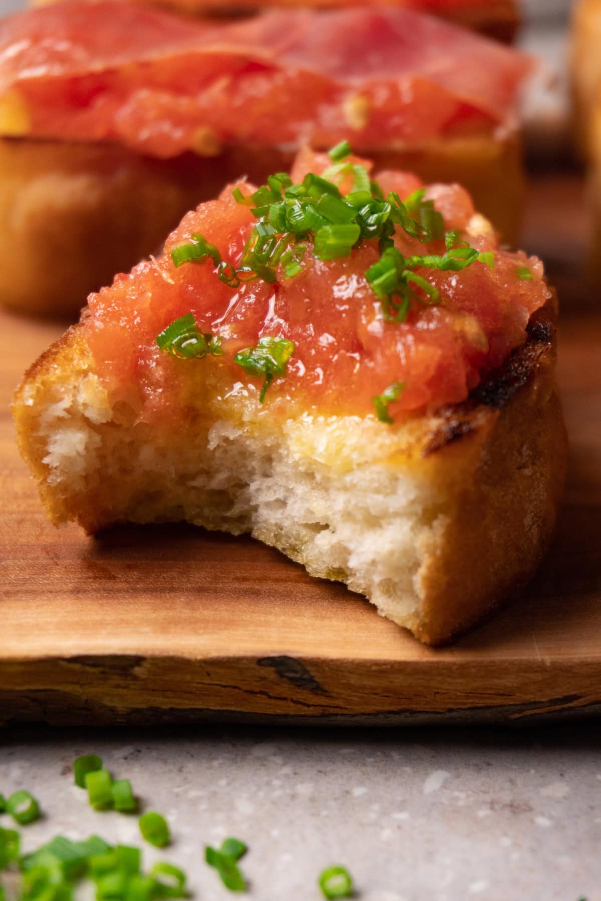 A piece of roasted bread with fresh tomato spread and chopped chives, with one bite taken.