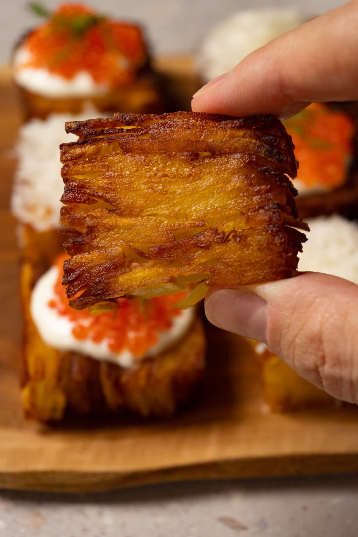 A hand is holding a golden, deep-fried piece of potato pavé.