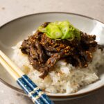 A bowl of rice and beef topped with sesame seeds and sliced green onions.
