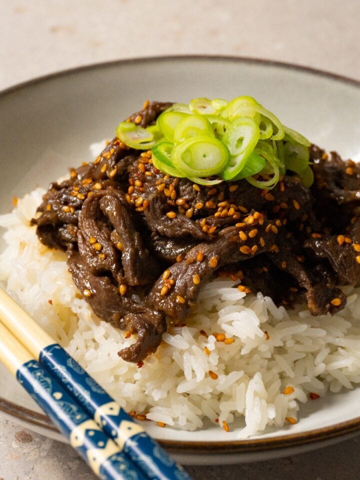 A bowl of rice and beef topped with sesame seeds and sliced green onions.